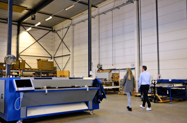 Beau, verpakkingsspecialist bij EBC Golfkarton, bekijkt samen met een logistiek manager in een magazijn een stapel dozen die scheef staat; ze maakt foto’s en bespreekt mogelijke verbeteringen.