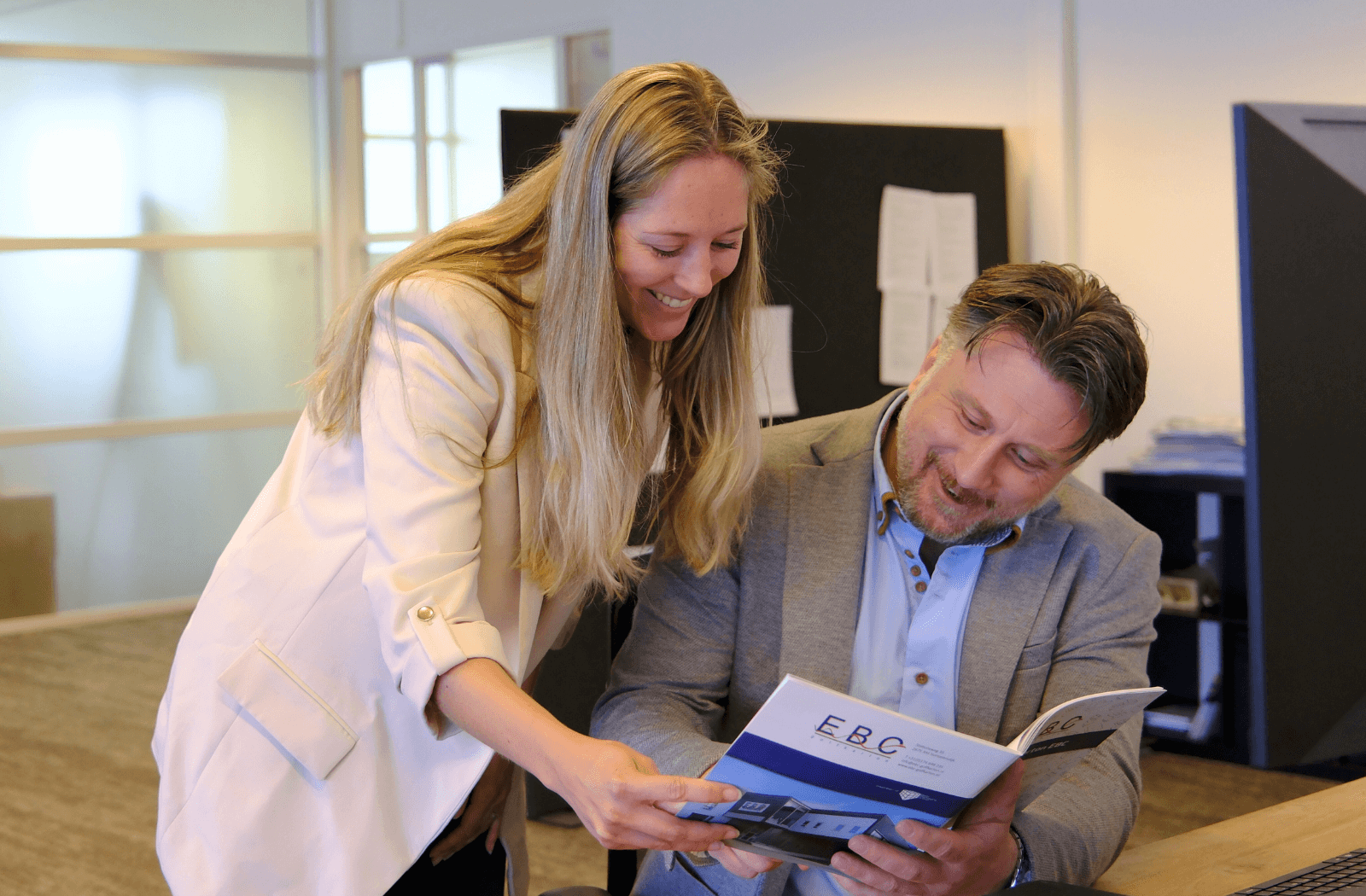 Beau, verpakkingsspecialist bij EBC Golfkarton, aan het werk tijdens een klantbezoek; hij bespreekt een maatwerk doosontwerp met een klant in een magazijn vol verpakkingen.